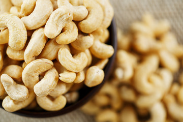 Cashew nuts in a wooden bowl on a burlap cloth background.