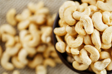 Cashew nuts in a wooden bowl on a burlap cloth background.