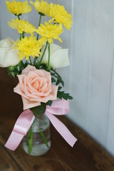 Lovely pinky blossom rose in vase on wooden table with white wall background, copy space