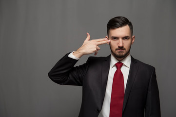 A bankrupt businessman in formal suit portrays suicide on gray background