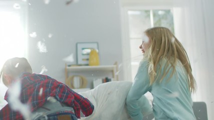 Adorable Little Boy and Sweet Little Girl Have a Pillow Fight in the Sunny Living Room. Siblings Having Fun Fighting with Pillows, Feathers Flying Around. In Slow Motion