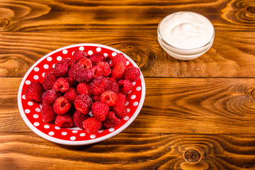 Ceramic plate with ripe raspberries and sour cream on wooden table