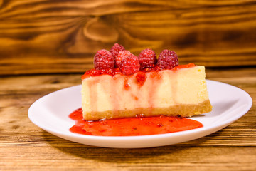 White plate with cheesecake New York and raspberries on wooden table