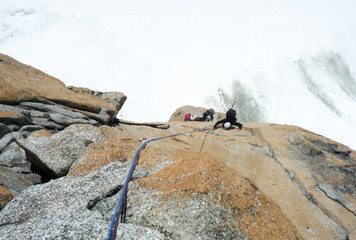 man rock climbing a steep vertical granite rock climbing route in the French Alps near Mont Blanc above white snow glacier