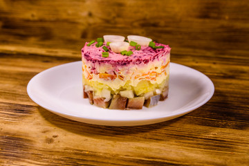 White plate with russian traditional new year salad herring under fur coat on wooden table
