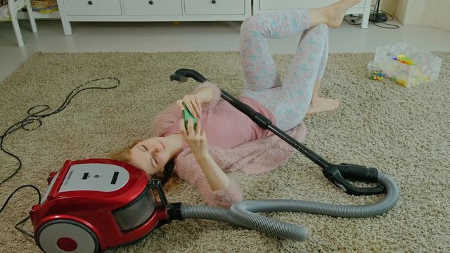 happy young woman or housewife with a vacuum cleaner, lying on the half-headphones, uses the phone, listens to music, dances, cleaning, housekeeping