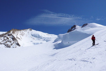 backcountry skier admires the view of the Monte Rosa mountains and glaciers in the Swiss Alps above Zermatt on a beautiful winter day