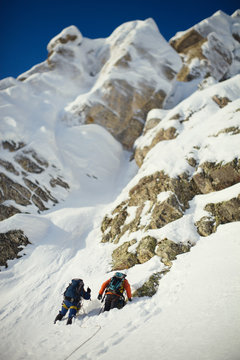Two climbers on a snow-covered mountain slope in the background rocky ridge. Tilt-shift effect.