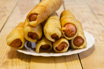 Delicious, flavorful sausages in the dough in a plate on a wooden table