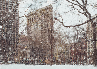 View of historic Flatiron building from Madison Square Park in New York City midtown Manhattan with snowflakes falling during winter snow storm - Powered by Adobe