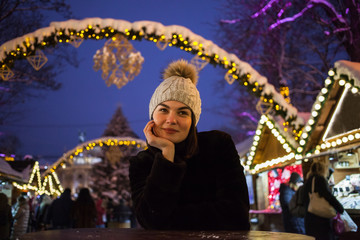 Young beautiful happy smiling girl posing in street. Festive Christmas fair on background.