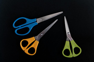 Three pairs of scissors (green blue and yellow) on black background