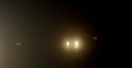Bright headlights of a car driving on foggy road
