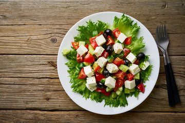 Greek salad on white plate on old rustic wooden table, top view, copy space