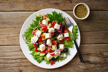 Greek salad on white plate on old rustic wooden table, top view