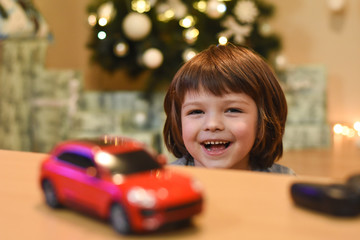 Happy boy play with car toys for Christmas. Smiling child having fun  and playing with cars. Colorful lights on background