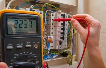 The wizard measures the voltage in the home network using a voltmeter. - obrazy, fototapety, plakaty