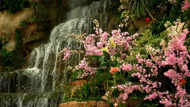 a large artificial waterfall framed by pink flowers and green leaves.