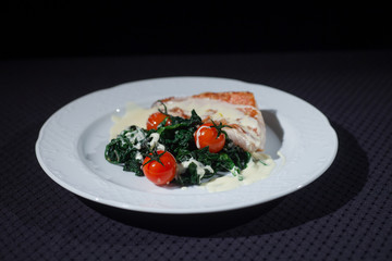 red fish sauce on a white plate on a black background with stewed greens and red tomatoes