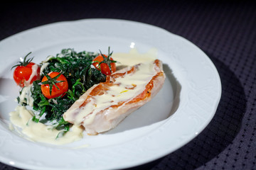 red fish sauce on a white plate on a black background with stewed greens and red tomatoes