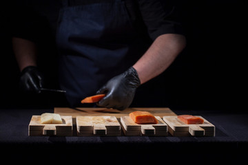 male hands in black gloves and a black apron on a black background cut the red fish on a wooden board