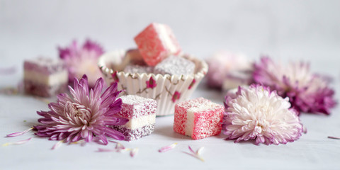 Fleet Ley cubes of fruit marmalade scattered on a white background with purple-colored chrysanthemum flower heads. Copy space
