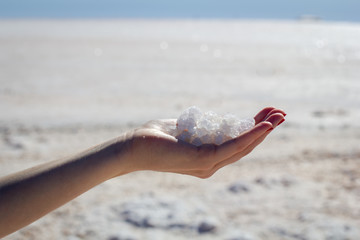 Female hand holding natural salt crystals on the background of a salt lake, side view