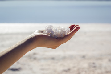 Female hand holding natural salt crystals on the background of a salt lake, side view