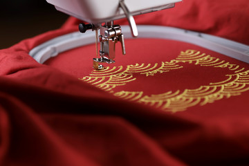 Embroidery of traditional shell pattern framing pig outline with gold on red fabric by modern embroidery machine - chinese new year concept - backside view on stitching area in studio light