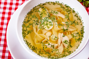Soup with chicken, quail egg and pasta in white bowl. Close up