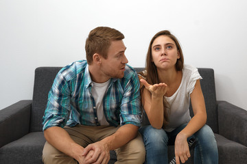 Portrait of long haired young woman with remote control reacting emotionally, making indignant gesture, pointing at TV screen while watching football game with her bearded boyfriend at home