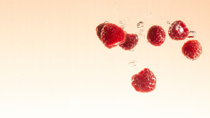 raspberry fruits making splash in water orange pastel background