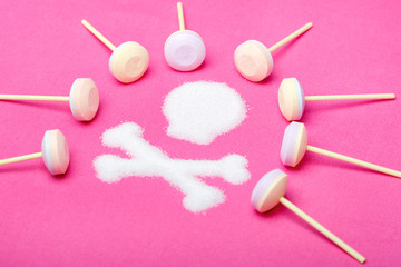 Several lollipops and a large skull and crossbones made of sugar grains. Shot on a pink background.