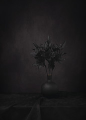 Black lilies in black vase shot against a black background.