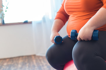 Chubby woman sport at home sitting on ball with dumbbells close-up