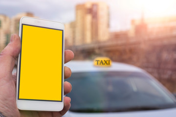 phone with a yellow screen in the hands of a man, a taxi car on the background of a blurred city.