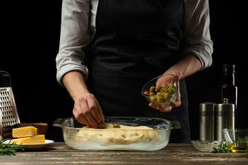 The chef prepares focaccia bread or pizza with olives, butter, cheese and rosemary greens. Recipe for home cooking from the chef. Background for design or menu