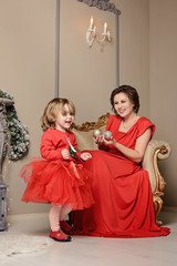 Happy young mother holds on the hands her cute baby girl on Christmas and New year holidays Child with mom in red dresses in the decorated room with Christmas tree and blurry festive lights