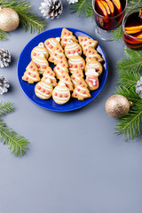 Tasty Christmas cookies, hot mulled wine and decorations with Christmas tree and lights on black background.