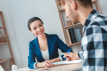 Man at real estate agency sitting signing contract with agent smiling happy