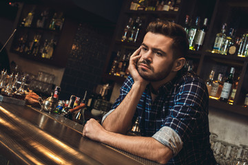 Young bartender leaning on bar counter bored close-up