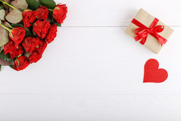 A bouquet of red roses, a gift and hearts on a white wooden table. Concept of Women's Day or St. Valentine. Copy space.