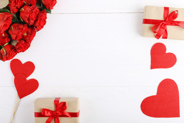 A bouquet of red roses, a gift and hearts on a white wooden table. Concept of Women's Day or St. Valentine. Copy space.
