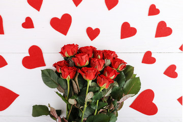 Red roses and hearts on a white wooden table. Concept of Women's Day or St. Valentine. Copy space.