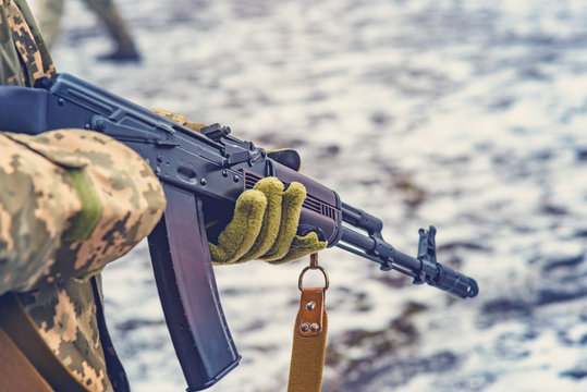 The gunman is holding a machine gun in winter mittens with his barrel down, after a hard and long battle, following the attack.