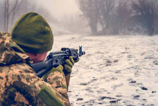 A military soldier with a Kalashnikov assault rifle conducts aimed fire at the enemy in winter, dressed in camouflage to prevent the enemy from advancing.