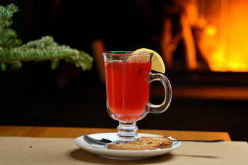 berry tea with lemon in a transparent glass on the background of the fireplace, Christmas tea