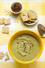 Vegetable soup with broccoli, served with crackers, linseed oil and seeds.