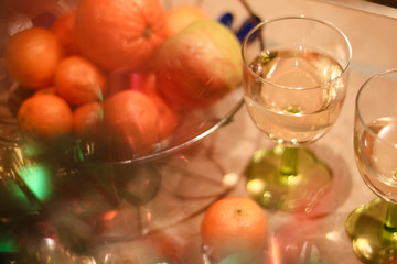New year's feast: two glasses of champagne and a basket with tangerines and apple on a beige table.