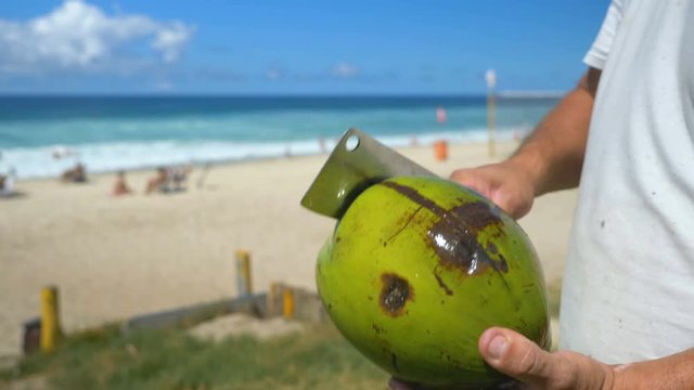 Man holding the chop knife to peeling and shelling a green fresh coconut on the beach, Rio de Janeiro